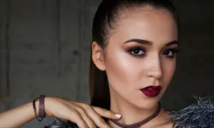 Kobieta z wyrazistym makijażem wieczorowym, ciemnymi ustami i smoky eyes. Długie włosy spięte w kucyk.
