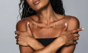 Kobieta z tatuażem na obojczyku "MY BODY MY RULES". Jej ramiona skrzyżowane na piersi, podkreślają siłę i niezależność.