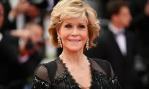 Uśmiechnięta Jane Fonda przed operacjami, w czarnej, ozdobnej sukni i długich kolczykach.