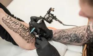 Artysta tworzy nowe tatuaże na rękę klienta, używając maszynki do tatuażu.