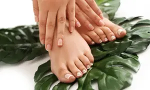 Dłonie i stopy z perfekcyjnym pedicure french na tle zielonych liści.