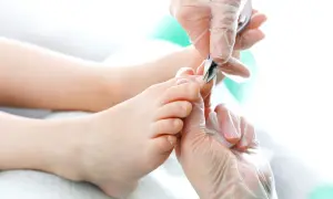 Dłonie w rękawiczkach precyzyjnie przycinają paznokcie u nóg. Pedicure w toku, dbałość o każdy szczegół.