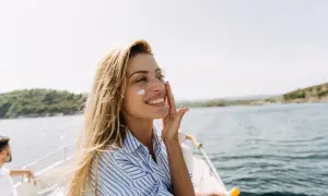 Uśmiechnięta blondynka na łodzi nakłada krem z filtrem, który nie tylko chroni, ale też co przyspiesza opalanie.