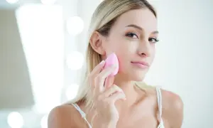 Blondynka z naturalnym pięknem, używa różowej gąbeczki do makijażu. Efekt make up no make up.