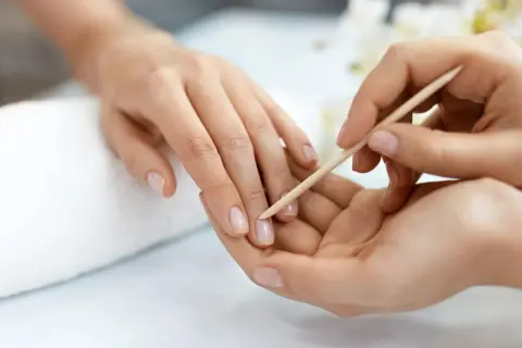 Delikatne dłonie poddawane zabiegowi manicure biologicznego. Skórki są starannie odsuwane patyczkiem, przygotowując paznokcie do dalszej pielęgnacji.