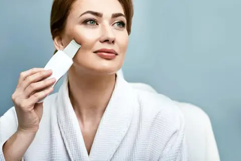 Kobieta w szlafroku wykonuje peeling kawitacyjny w domu, odświeżając cerę.