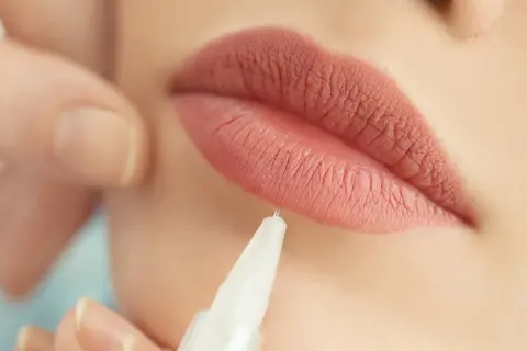 Zbliżenie na usta podczas zabiegu makijażu permanentnego. Delikatna igła zbliża się do perfekcyjnie podkreślonej linii ust.