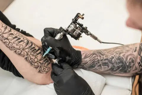 Artysta tworzy nowe tatuaże na rękę klienta, używając maszynki do tatuażu.