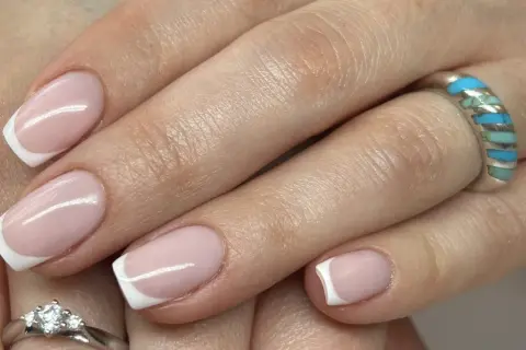 Dłonie z klasycznym french manicure, zdobione subtelnym wzorkiem. Na palcach błyszczą pierścionki.