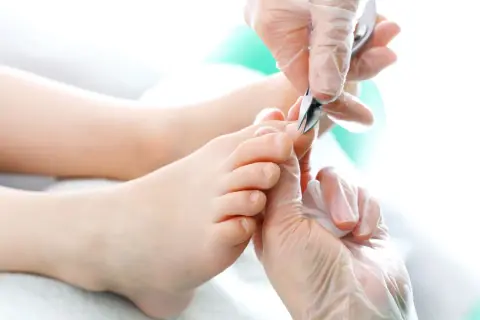 Dłonie w rękawiczkach precyzyjnie przycinają paznokcie u nóg. Pedicure w toku, dbałość o każdy szczegół.