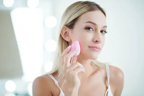 Blondynka z naturalnym pięknem, używa różowej gąbeczki do makijażu. Efekt make up no make up.