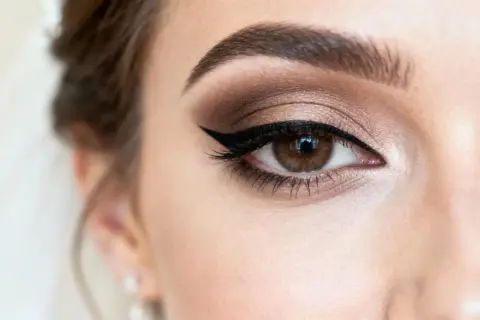Oko z perfekcyjnym makijażem glamour: brązowe cienie, kreska typu kocia i wytuszowane rzęsy.