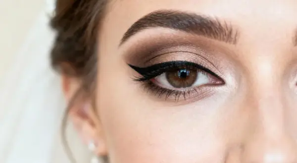 Oko z perfekcyjnym makijażem glamour: brązowe cienie, kreska typu kocia i wytuszowane rzęsy.