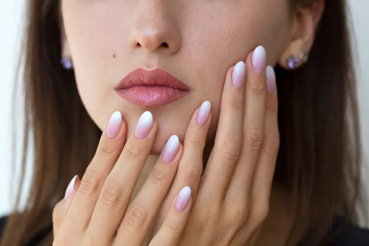 Delikatne baby boomer nails na dłoniach kobiety, z subtelnym ombre od różu do bieli.
