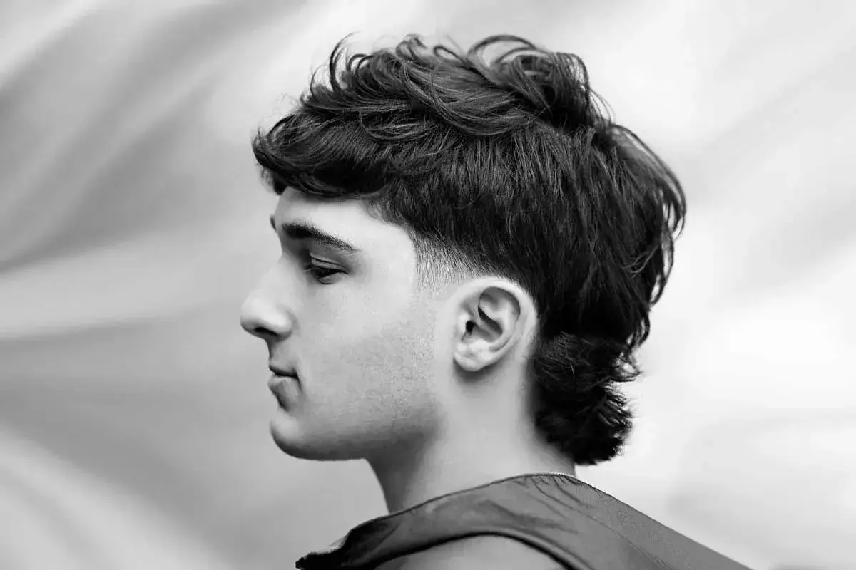 Czarno-białe zdjęcie mężczyzny z nowoczesną fryzurą typu mullet, widok z profilu.