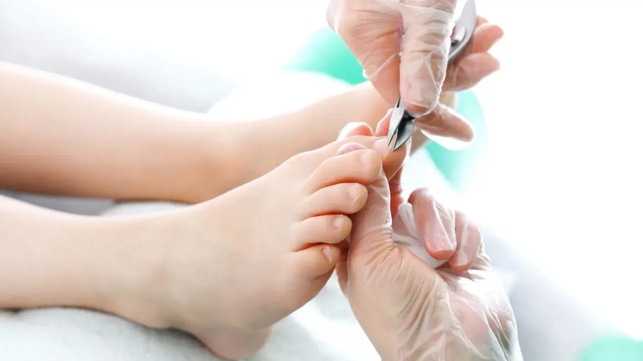 Dłonie w rękawiczkach precyzyjnie przycinają paznokcie u nóg. Pedicure w toku, dbałość o każdy szczegół.
