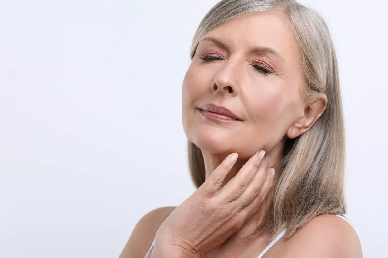 Kobieta z zamkniętymi oczami, dotykająca szyi. Widać delikatne zmarszczki marionetki, świadczące o upływie czasu.