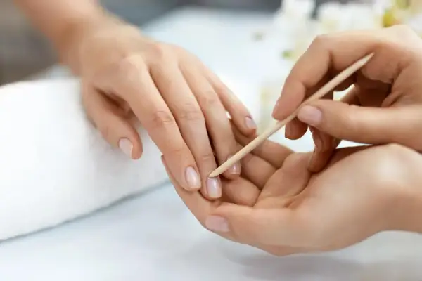 Delikatne dłonie poddawane zabiegowi manicure biologicznego. Skórki są starannie odsuwane patyczkiem, przygotowując paznokcie do dalszej pielęgnacji.
