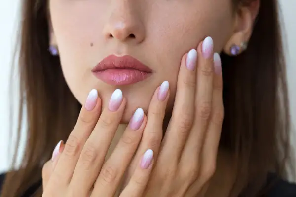 Delikatne baby boomer nails na dłoniach kobiety, z subtelnym ombre od różu do bieli.