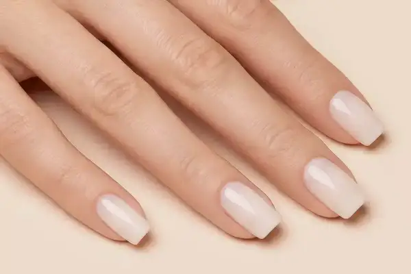 Dłoń z idealnie zadbanymi, klasycznymi paznokciami w mlecznym kolorze. Delikatny manicure podkreśla naturalne piękno.