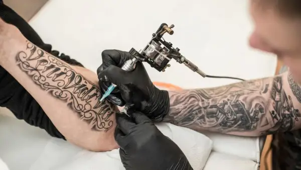 Artysta tworzy nowe tatuaże na rękę klienta, używając maszynki do tatuażu.