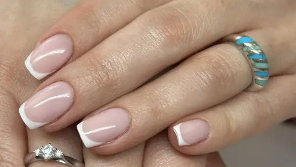 Dłonie z klasycznym french manicure, zdobione subtelnym wzorkiem. Na palcach błyszczą pierścionki.